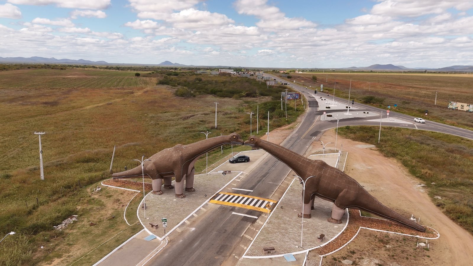 Vista aérea do portal de Sousa, na Paraíba, com duas esculturas de dinossauro sobre a rodovia e o sertão em volta