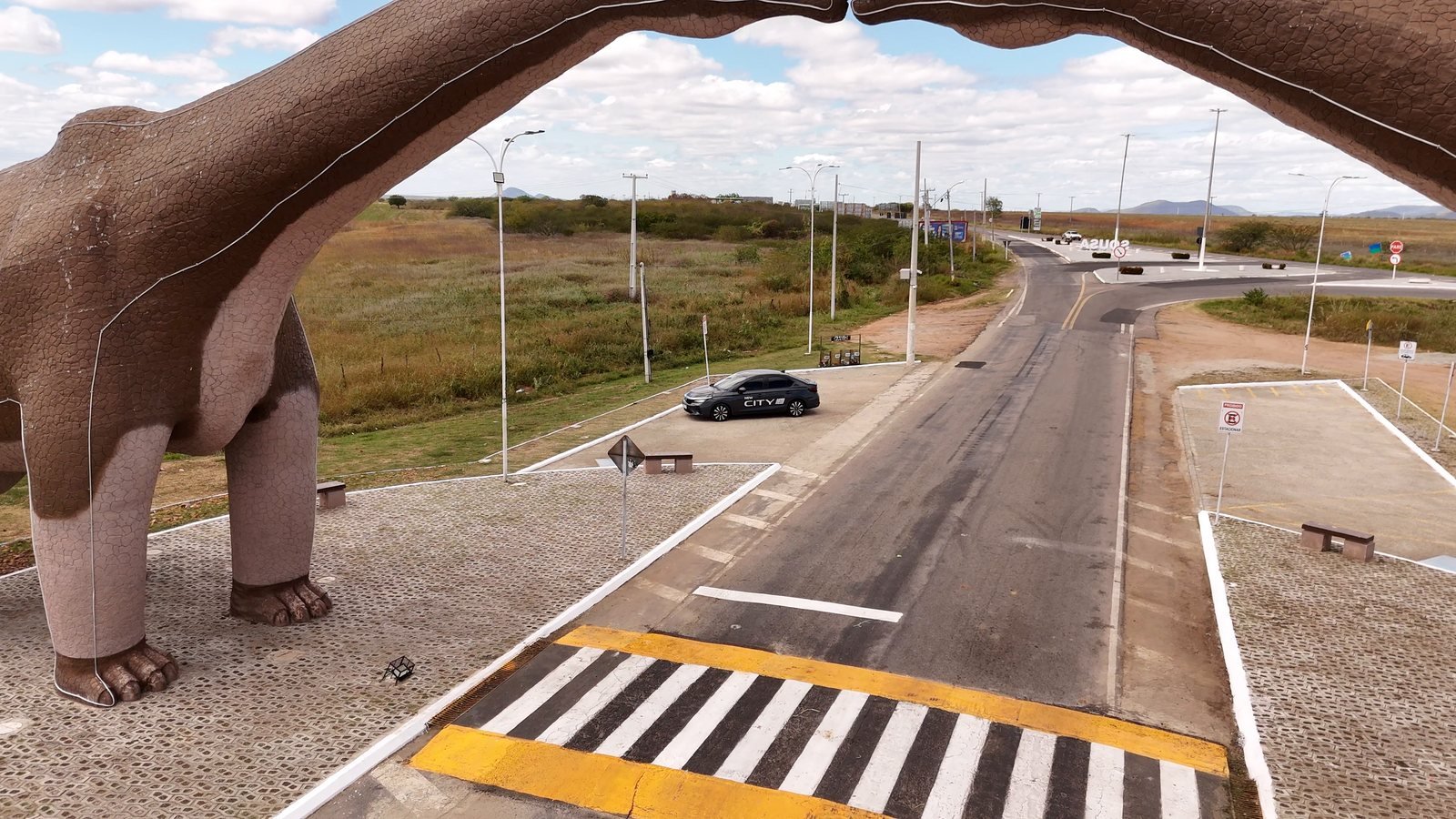 Portal de Sousa visto do alto, passando por baixo do pescoço de uma das esculturas de dinossauro, com a rodovia embaixo