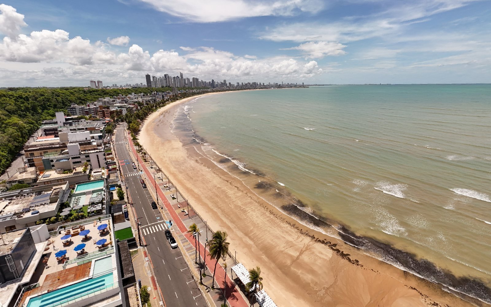 Vista aérea do fim da praia do Cabo Branco, com a curva da orla e os prédios de João Pessoa ao fundo