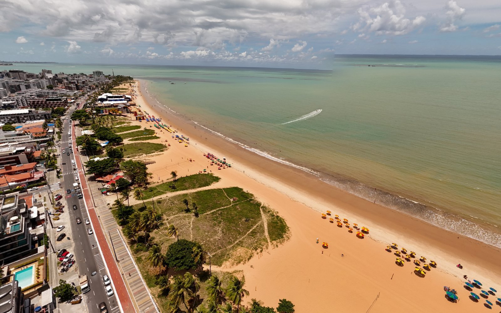 Vista aérea da praia do Cabo Branco, em João Pessoa, com guarda-sóis coloridos na areia, coqueiros, a ciclovia vermelha e a avenida da orla