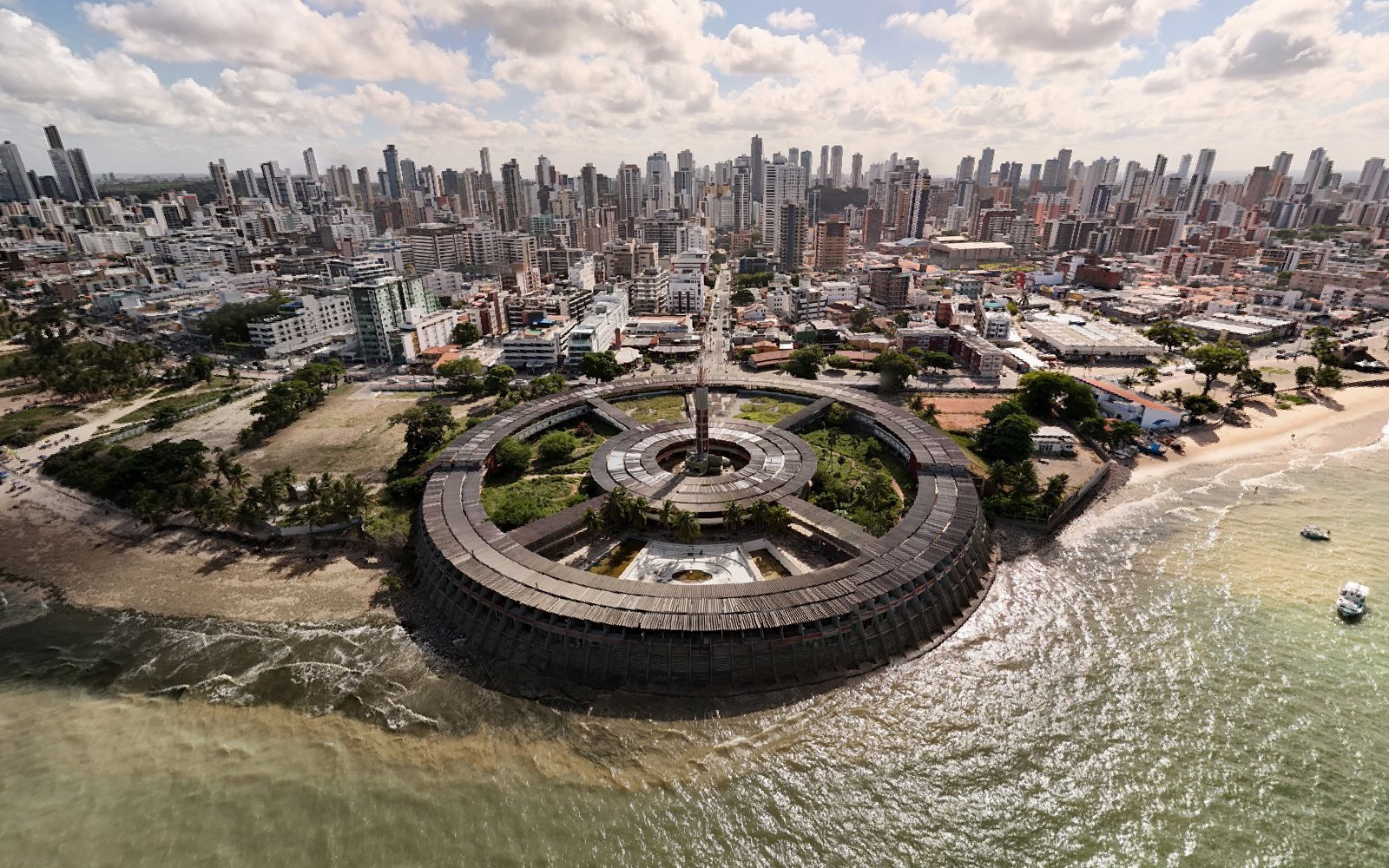Vista aérea do Hotel Tambaú, o prédio circular avançando sobre o mar, com a praia de Tambaú e os prédios de João Pessoa ao fundo