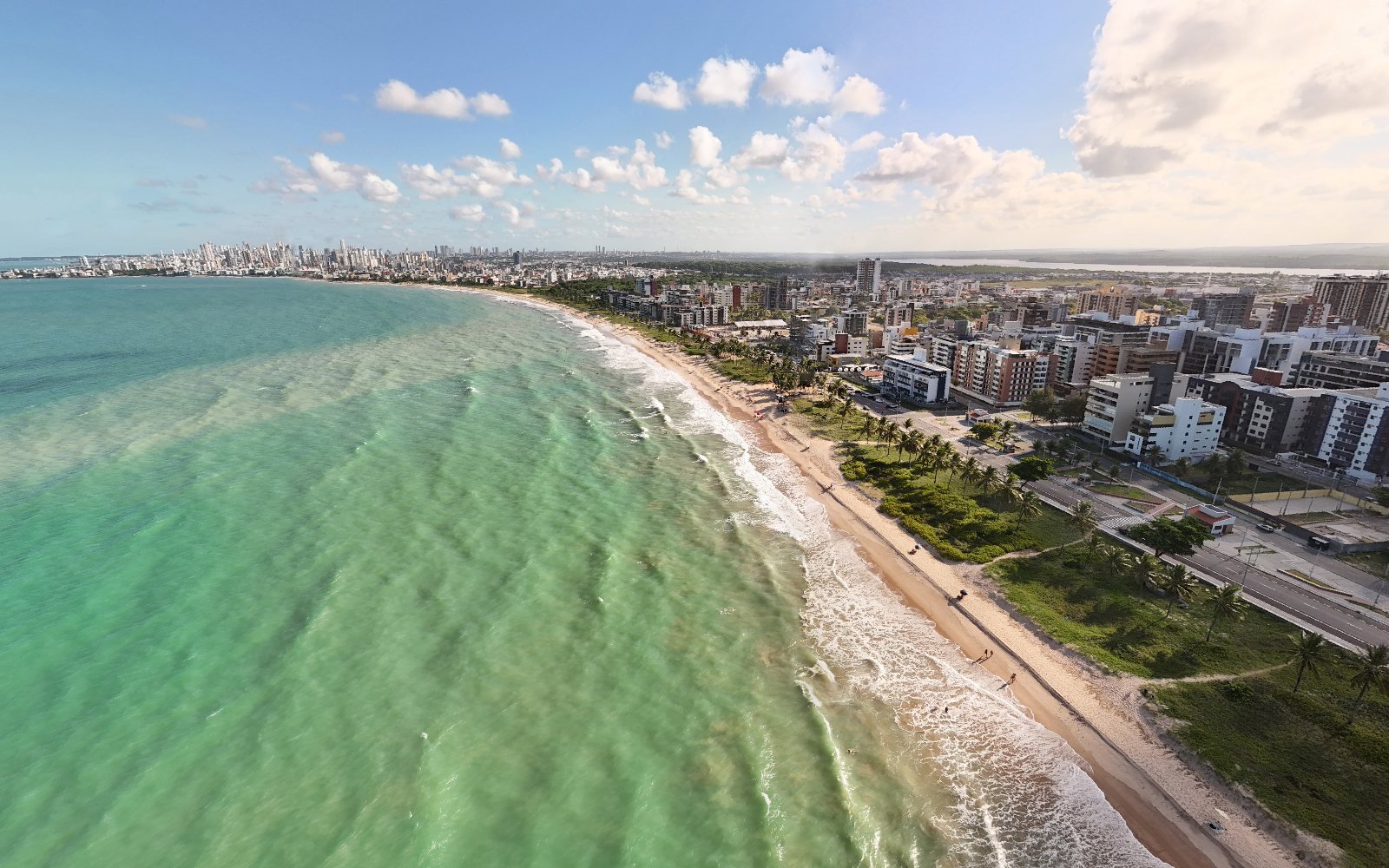 Vista aérea da praia de Intermares, em Cabedelo, com a faixa de areia curvando e a orla de João Pessoa ao fundo