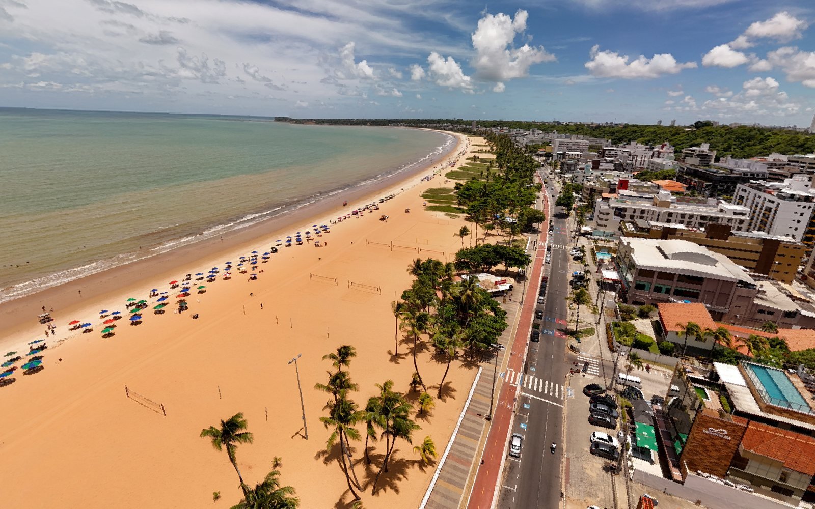Vista aérea da praia do Cabo Branco, em João Pessoa, com guarda-sóis na areia, coqueiros e a ciclovia
